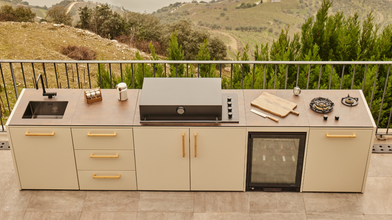 Cocina de exterior Brabura Grills modular con fregadero, barbacoa integrada, vinoteca y quemadores de gas en una terraza con vistas al campo
